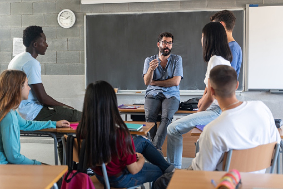 Docente conversa con estudiantes sentados en círculo dentro del aula.