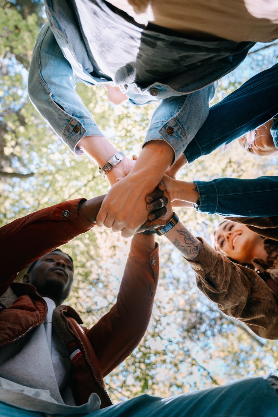 Grupo de personas uniendo las manos al aire libre, visto desde abajo.